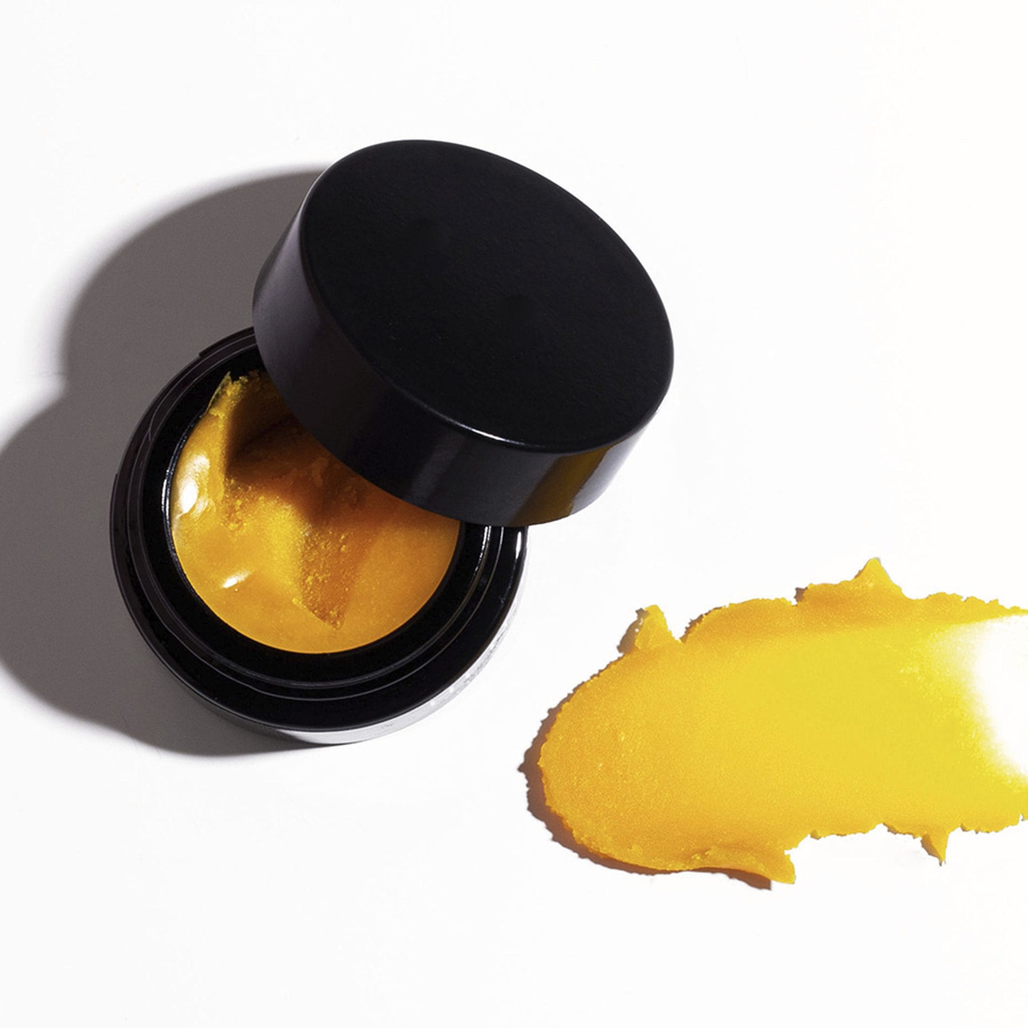 Open Henné Organics Lip Mask jar beside a swatch of the rich golden balm texture