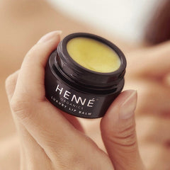 Hand holding an open jar of Henné Organics Luxury Lip Balm with smooth natural balm inside