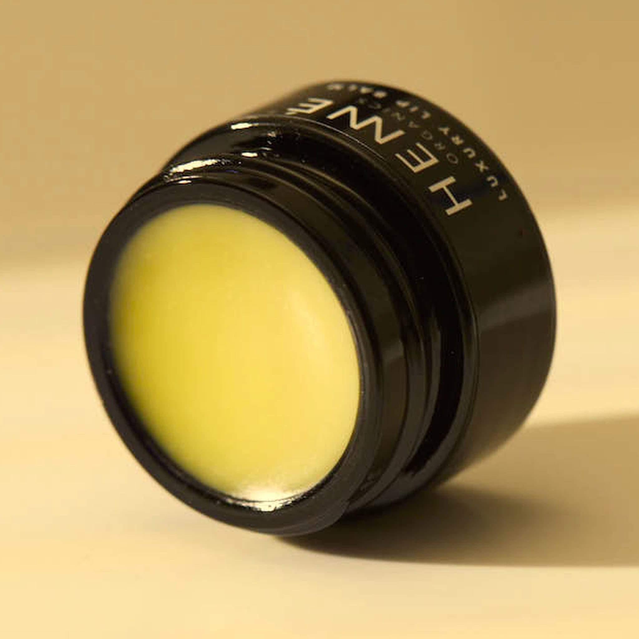 Open jar of Henné Organics Luxury Lip Balm tilted in warm golden light showing the buttery balm