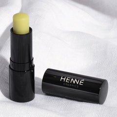 Uncapped Henné Organics Luxury Lip Balm stick and black cap resting on soft white linen