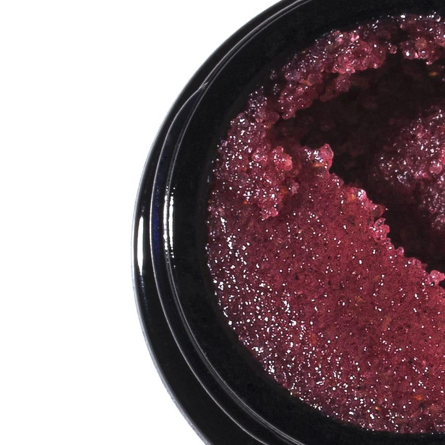 Close-up of glossy berry red sugar lip scrub inside a black glass jar