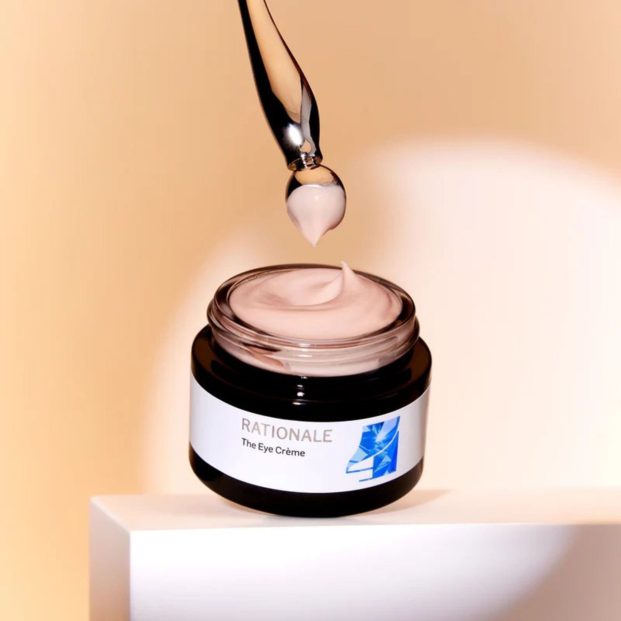 Rationale The Eye Crème open jar with dropper applicator showing pink cream texture on warm beige background