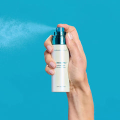 Hand holding a bottle of Colorescense Barrier Pro Serum against a blue background