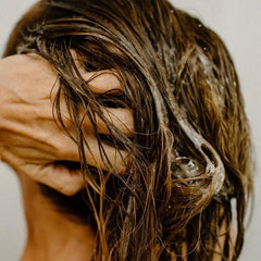 Person with wet hair covering their face against a neutral background