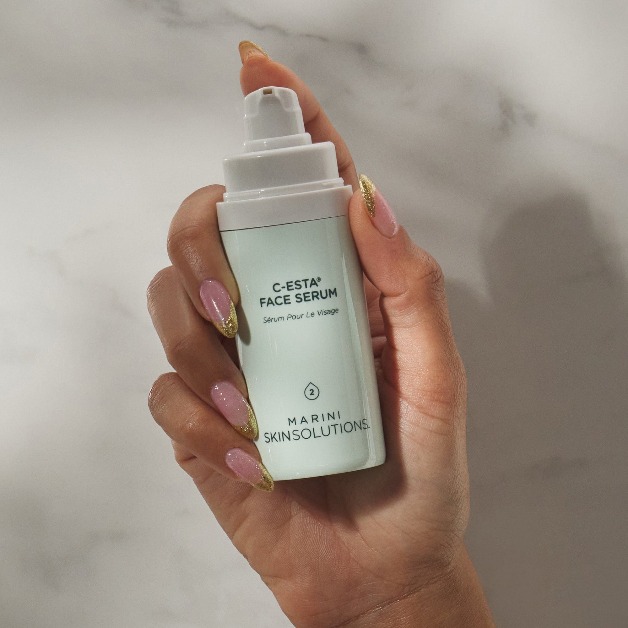Hand holding a bottle of C-Esta Face Serum by Marini Skinsolutions against a marble background