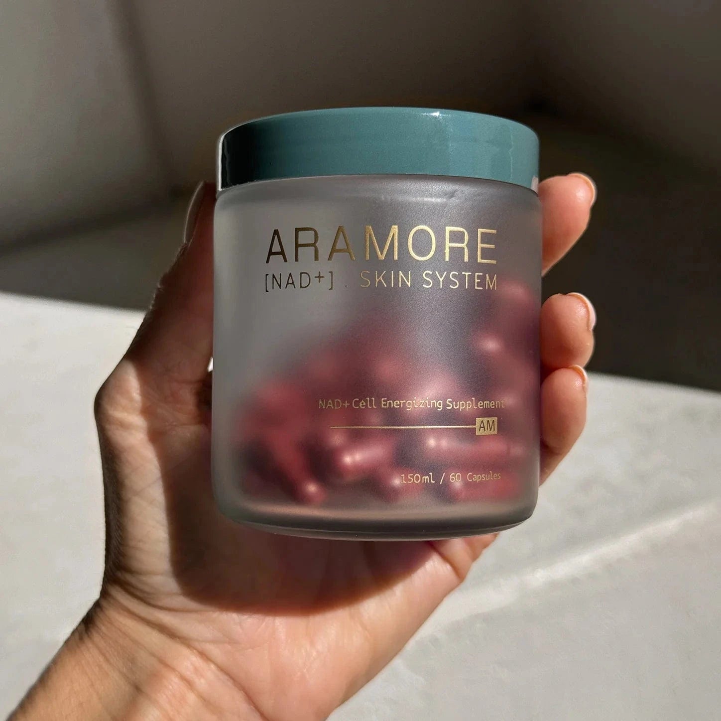 Hand holding a jar of Aramore Skin System supplement with a blurred background