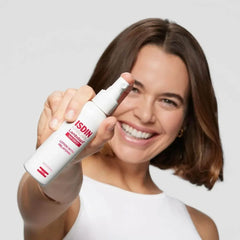 Woman holding an ISDIN bottle against a light gray background