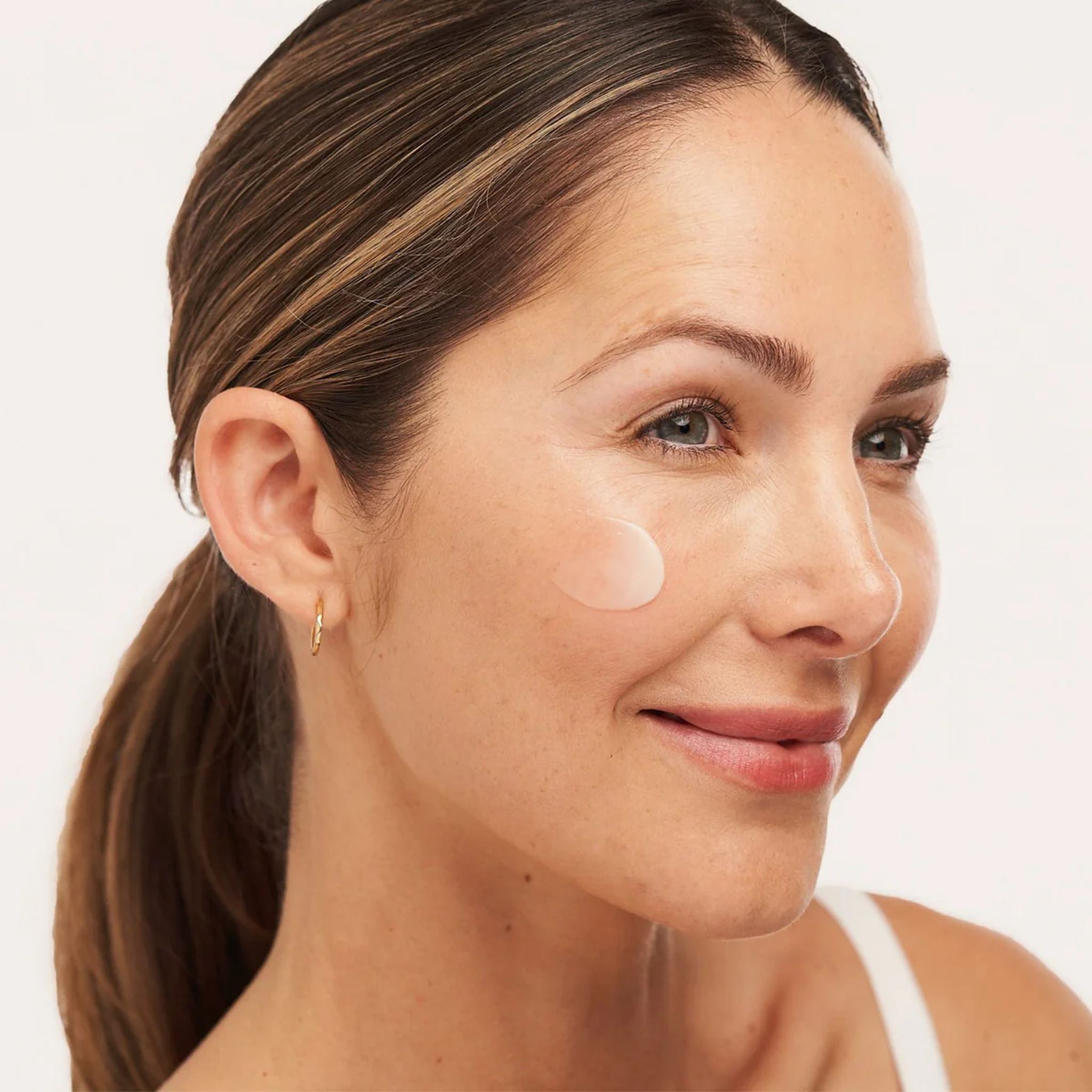 Woman with ALASTIN C-Radical Defense Antioxidant Serum applied to her cheek for bright protected skin