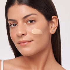 Woman with a swipe of ALASTIN HydraTint tinted mineral sunscreen on her cheek showing its sheer glowing tint
