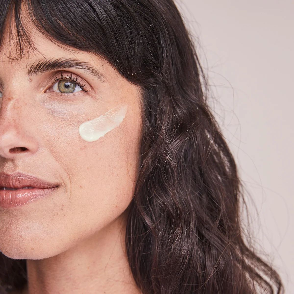 Woman with a swipe of ALASTIN Renewal Retinol serum on her cheek showing its light creamy texture