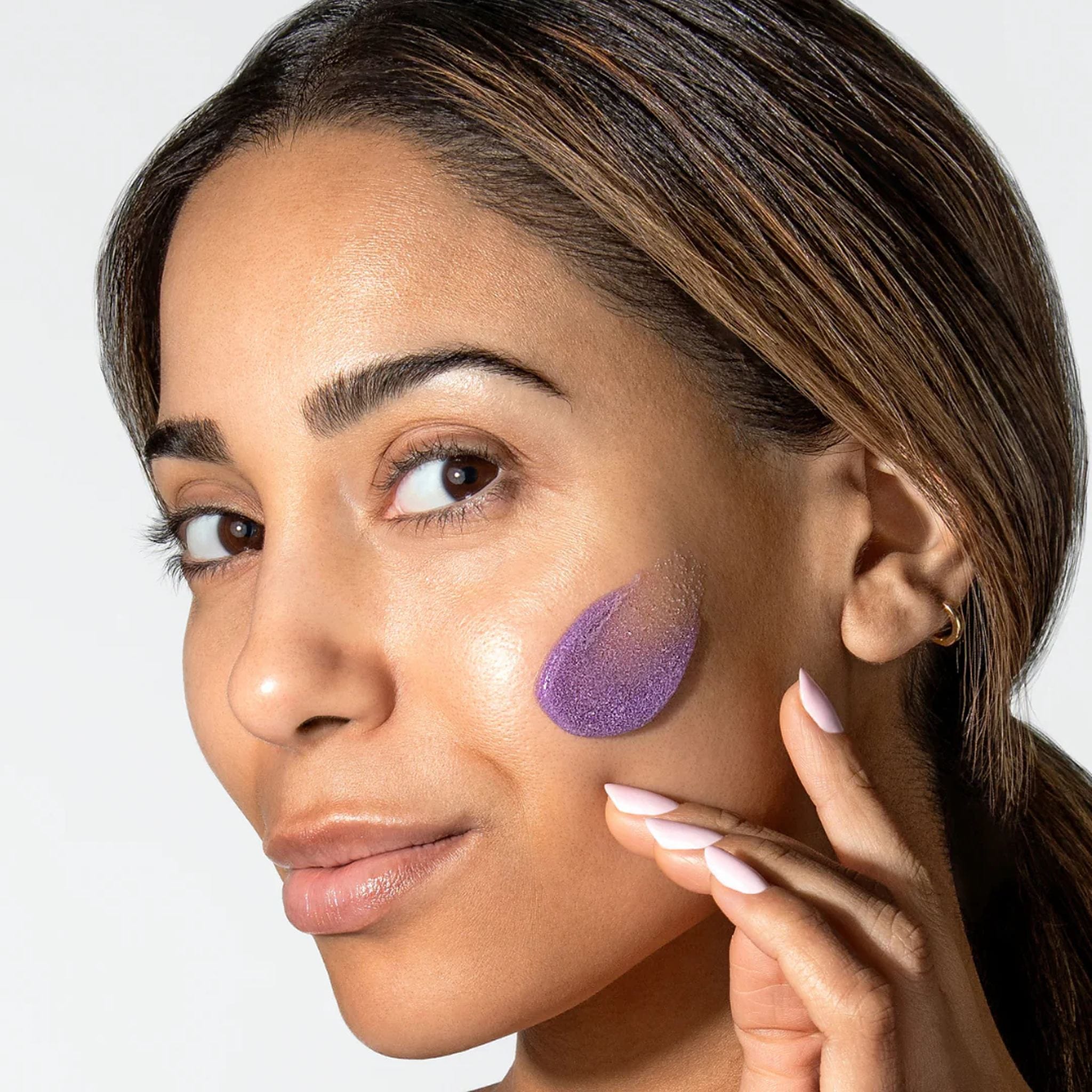 Woman with ALASTIN ReSURFACE Skin Polish purple exfoliating scrub applied to cheek