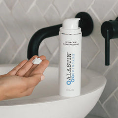 ALASTIN Ultra Calm Cleansing Cream pump bottle on a bathroom sink beside a hand holding a dollop of cream