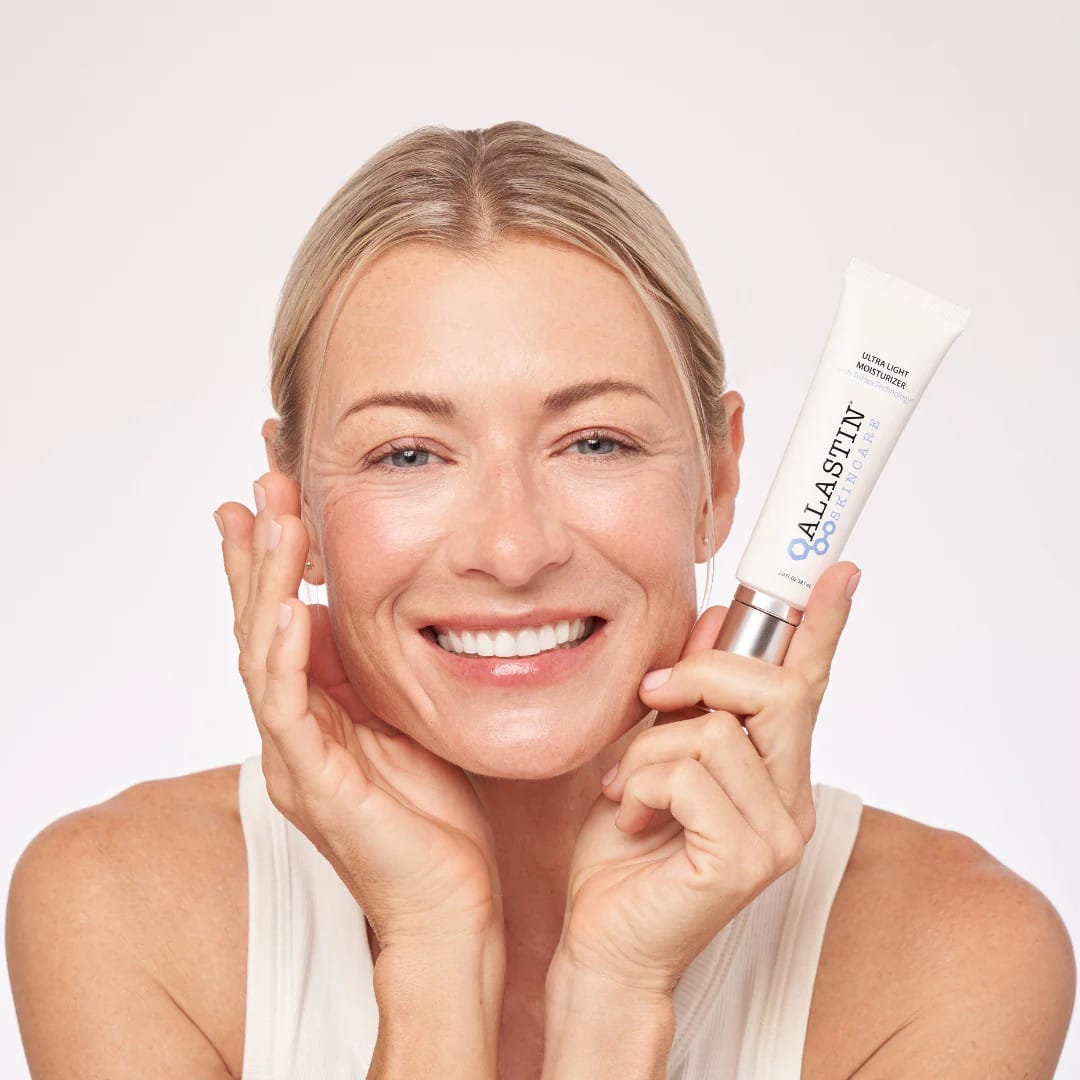 Smiling woman holding ALASTIN Ultra Light Moisturizer tube beside her face