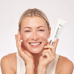 Smiling woman holding ALASTIN Ultra Light Moisturizer tube beside her face