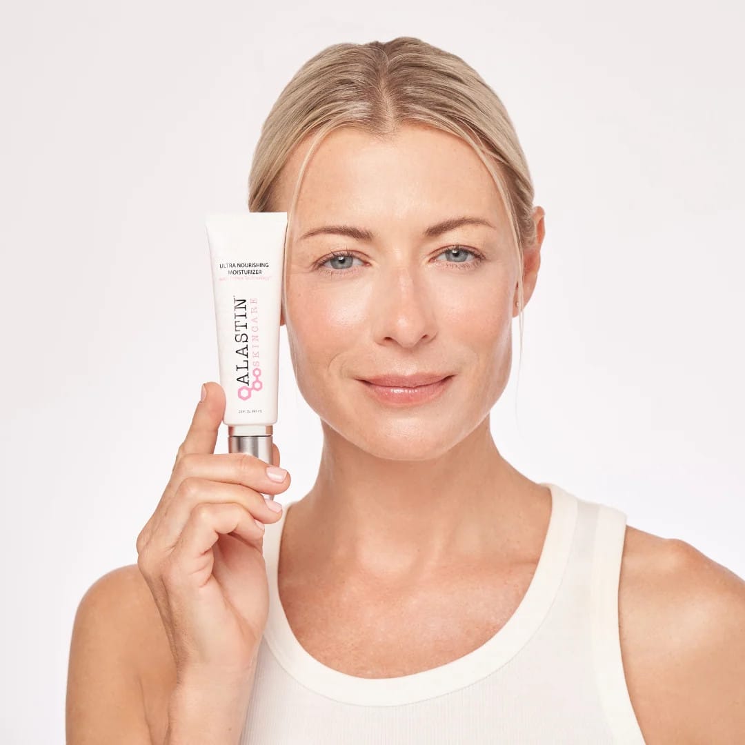Woman with glowing skin holding ALASTIN Ultra Nourishing Moisturizer tube beside her face