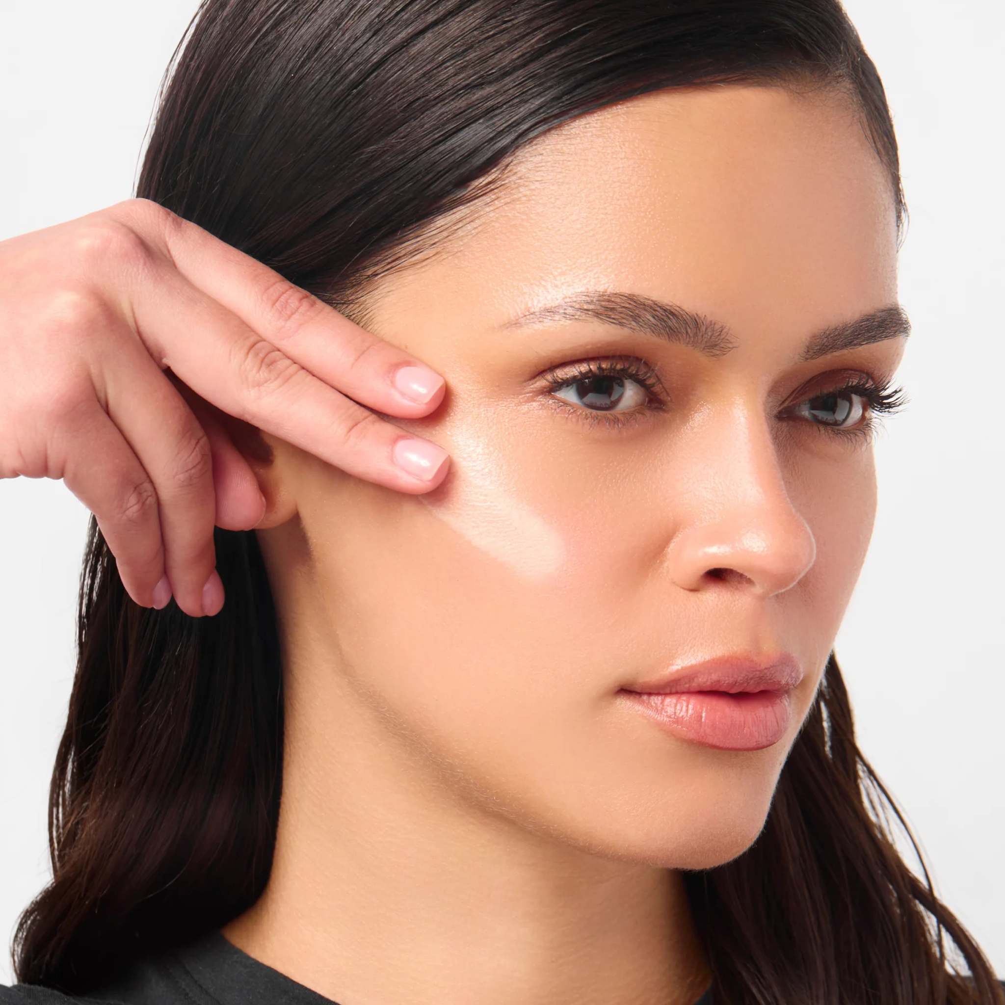 Woman with dark hair pressing peptide lifting serum into her cheekbone for a dewy glow