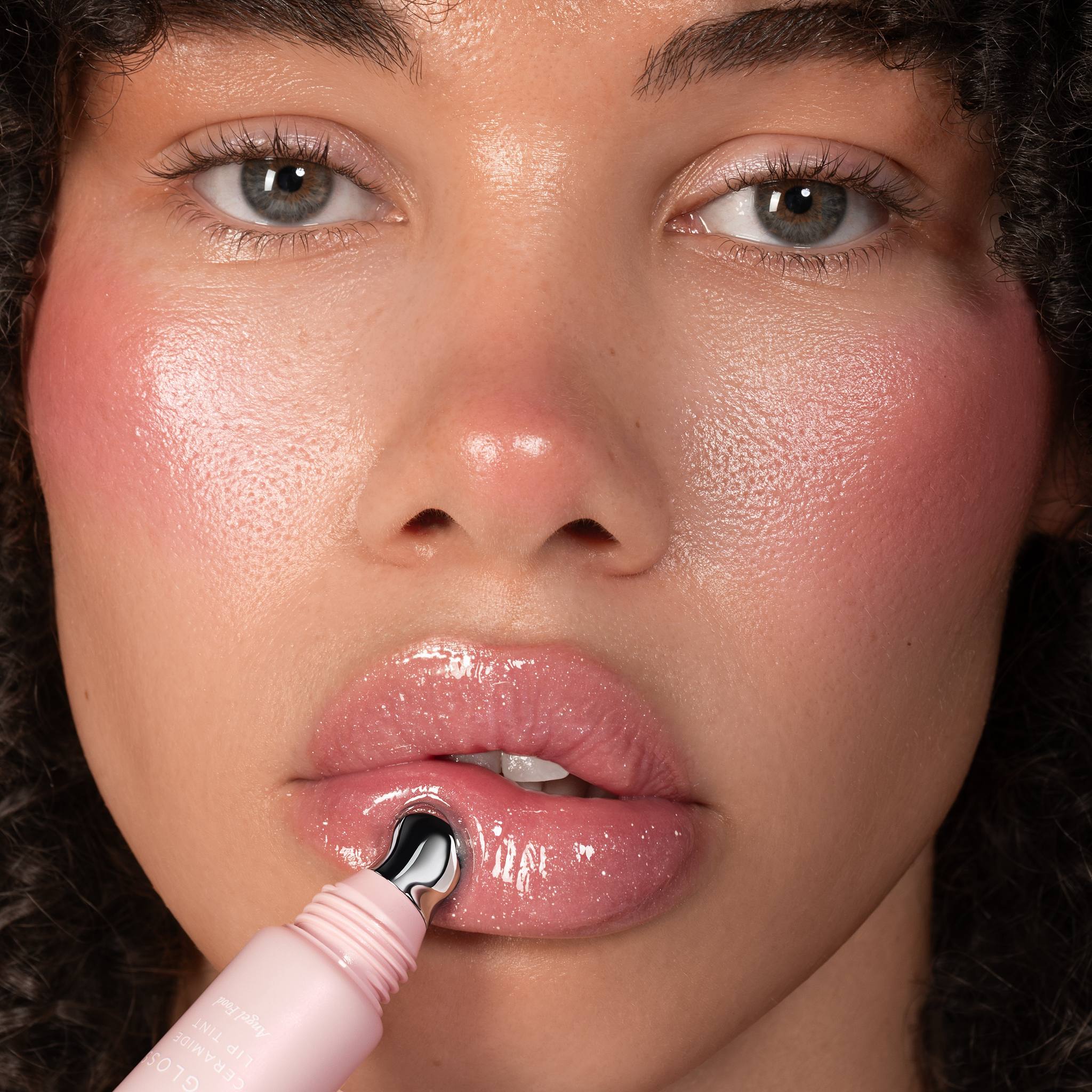 Model with curly hair applying Anfisa Skin AN-Gloss Ceramide Lip Tint Angel Food with roller applicator 3