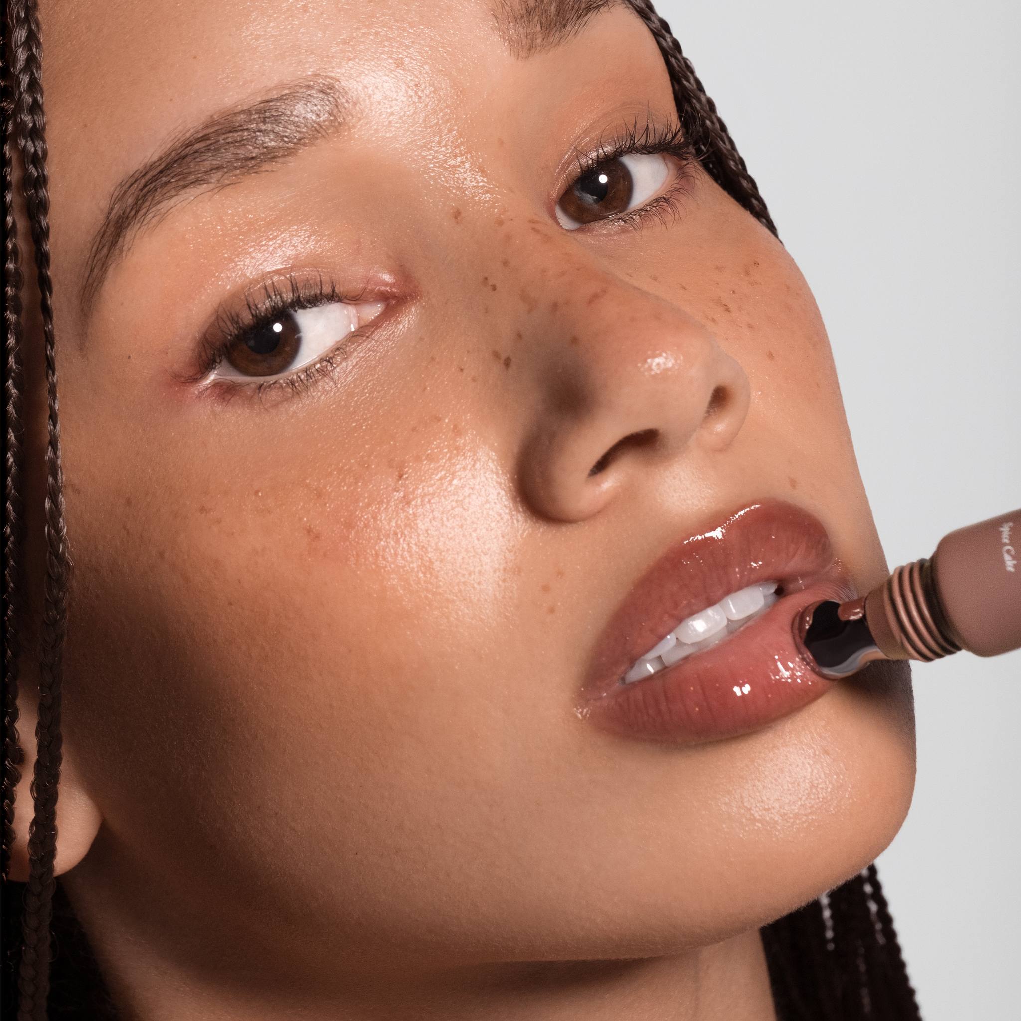 Model with braids applying Anfisa Skin AN-Gloss Ceramide Lip Tint in Spice Cake with roller applicator 3