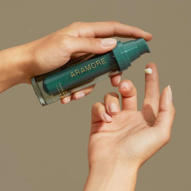 Hand holding a green bottle labeled 'Aramore' against a beige background