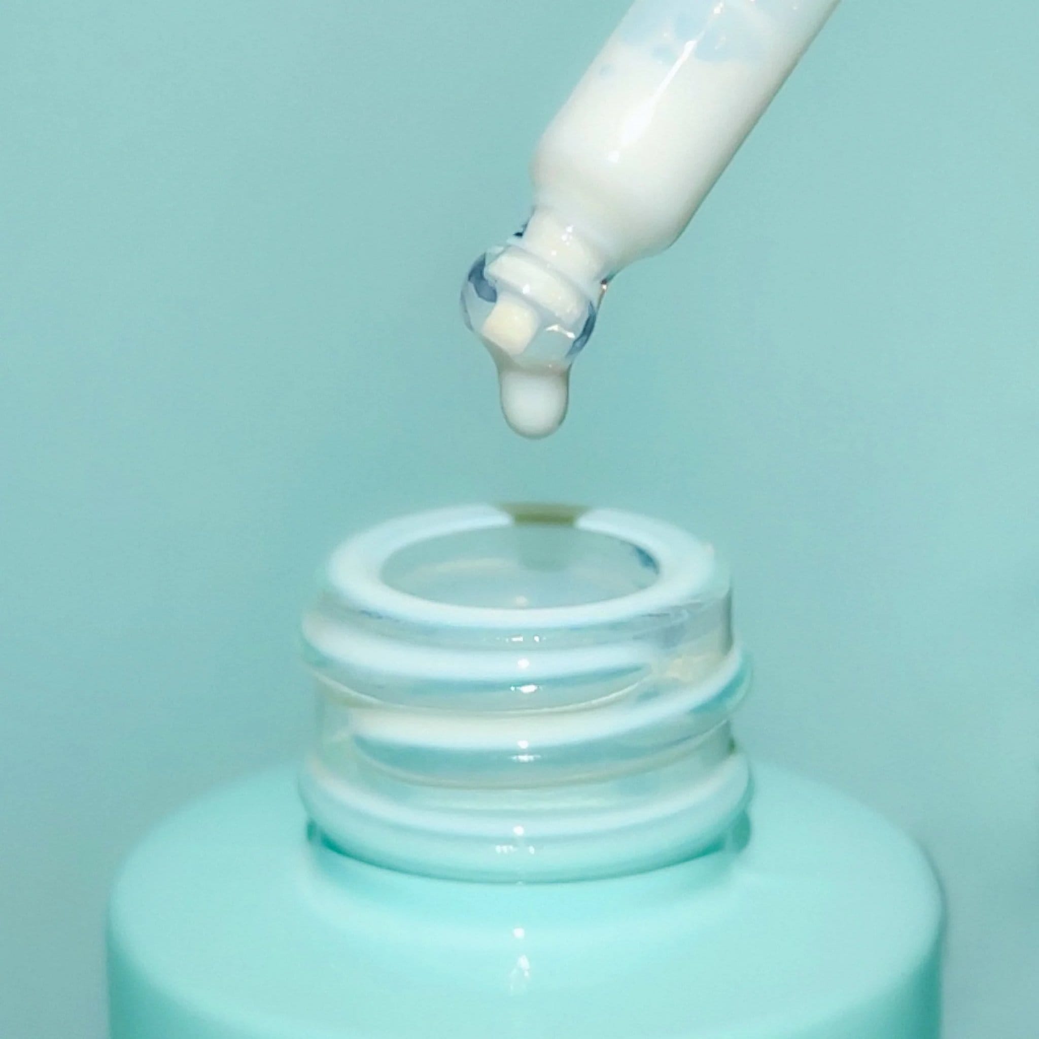 Closeup of Bask mineral sunscreen serum SPF 30 dropper pipette dispensing a single drop above open bottle