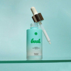 Bask SPF 30 mineral sunscreen serum open frosted bottle with dropper leaning against it on teal surface