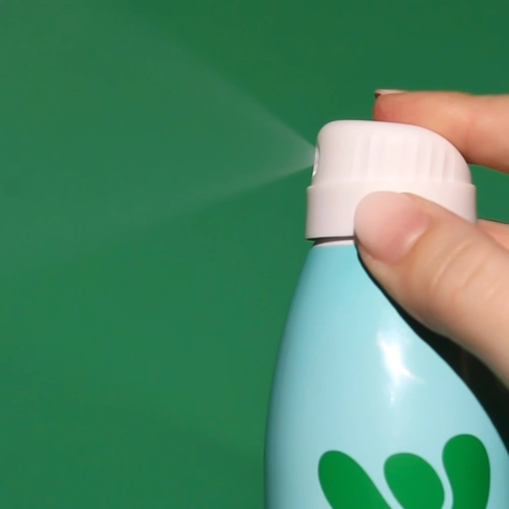 Closeup of Bask mineral sunscreen spray nozzle being pressed showing fine continuous mist on green background