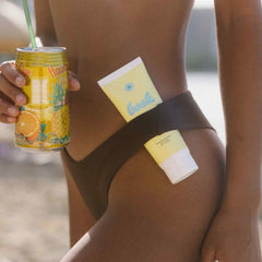 Model at beach holding Bask SPF 30 sheer moisturizing sunscreen lotion tube and tropical drink outdoors
