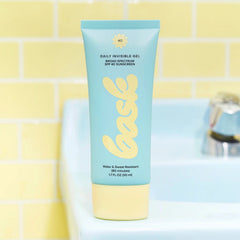 Bask SPF 40 daily invisible gel sunscreen tube standing on bathroom sink with yellow tile background
