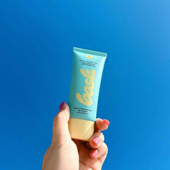 Hand holding Bask SPF 40 daily invisible gel sunscreen tube against vivid blue sky background