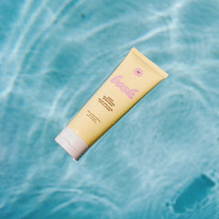 Bask SPF 50 sheer moisturizing sunscreen lotion tube floating in sparkling blue pool water