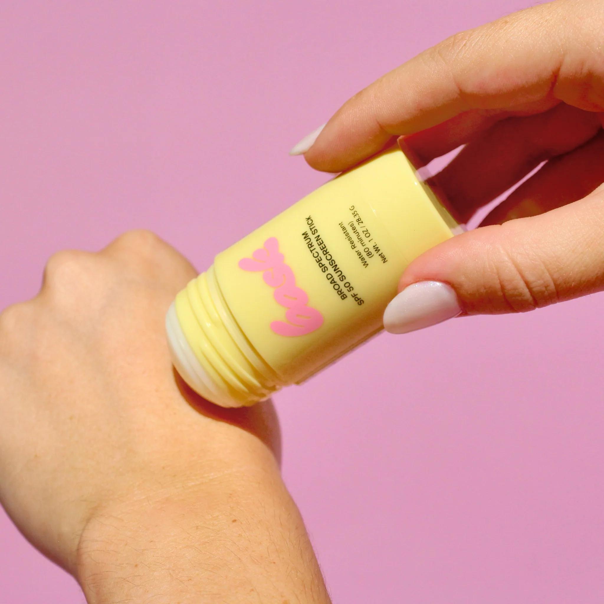 Bask SPF 50 sunscreen stick being applied to wrist showing easy glide stick application on purple background