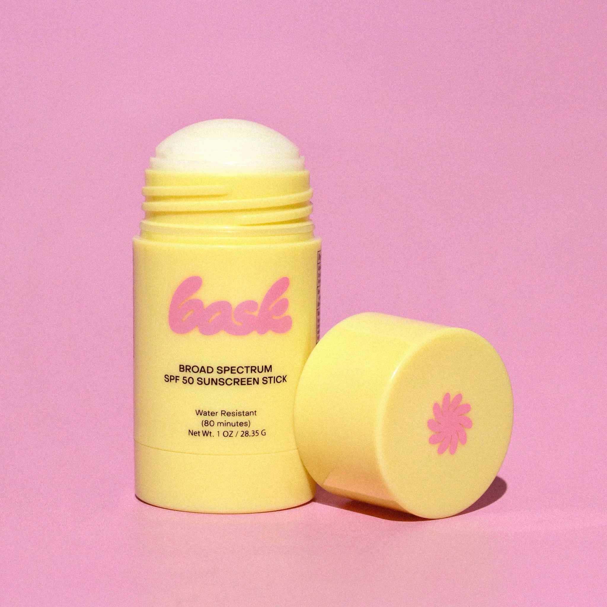 Bask SPF 50 sunscreen stick open with cap beside it showing pink logo and daisy on yellow tube