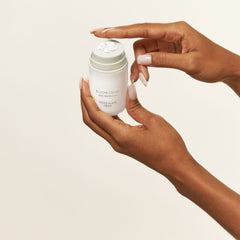 Hands holding open Bloom Cream jar with whipped moisturizer texture on top