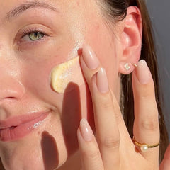 Woman applying Milk Scrub exfoliating cleanser with visible jojoba beads to cheek