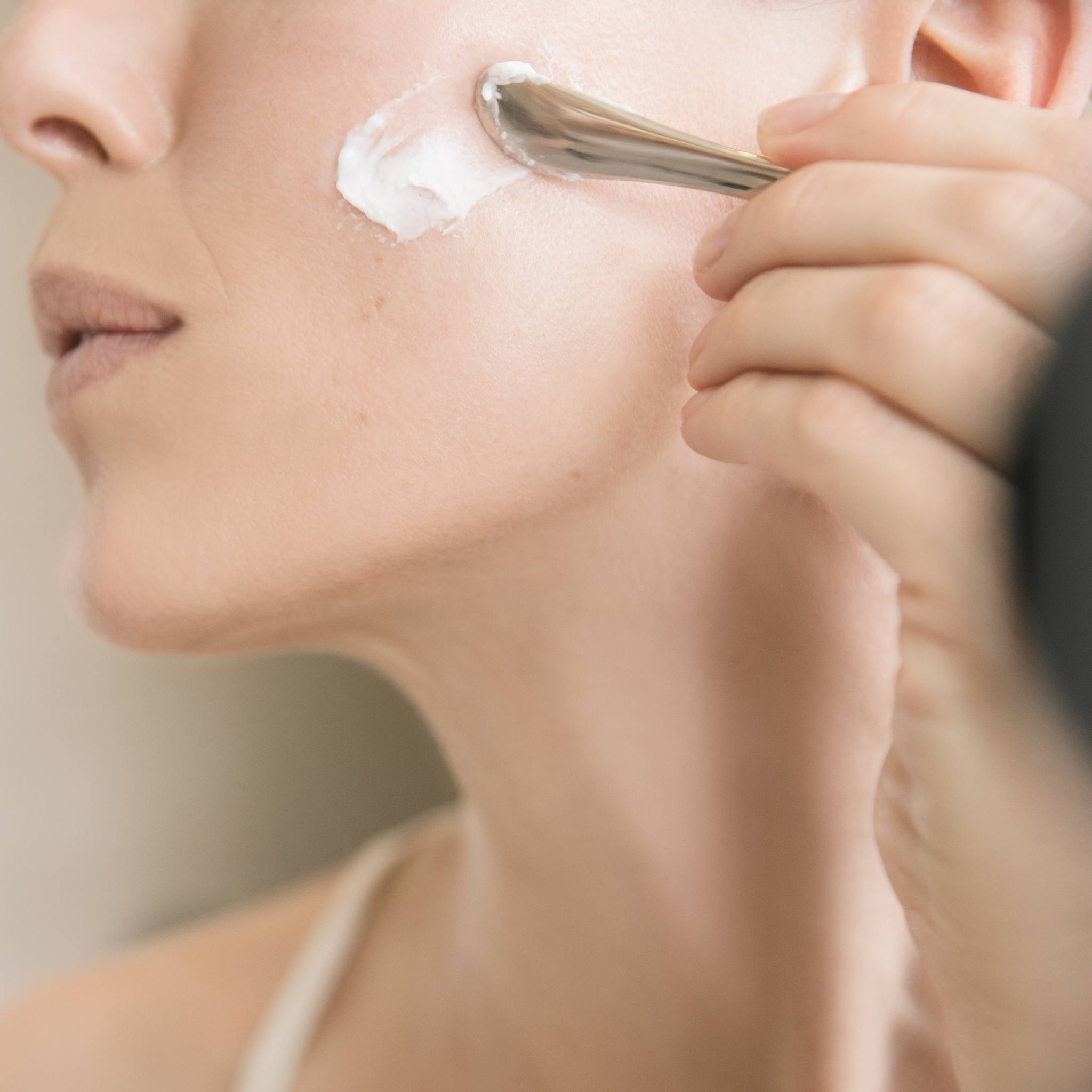 Close-up of BIOEFFECT EGF Power Cream being applied to cheek with metal spatula showing anti-aging cream texture