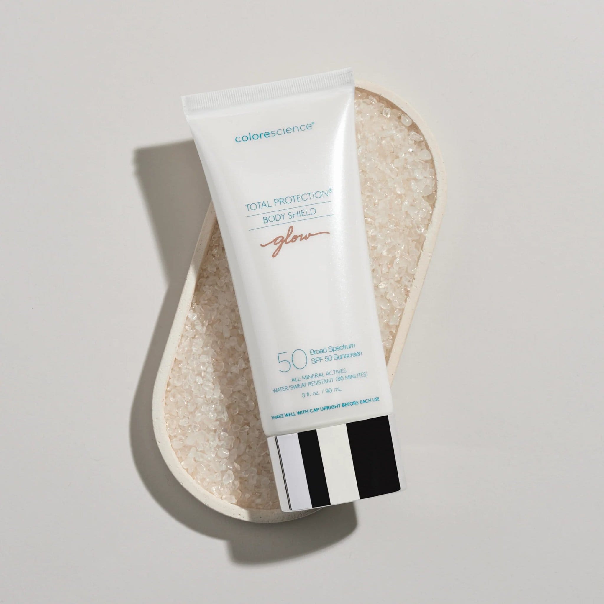 Colorescience Body Shield Glow SPF 50 sunscreen tube resting on sea salt crystals in dish