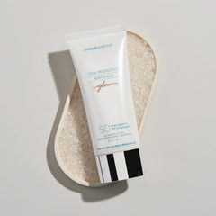 Colorescience Body Shield Glow SPF 50 sunscreen tube resting on sea salt crystals in dish