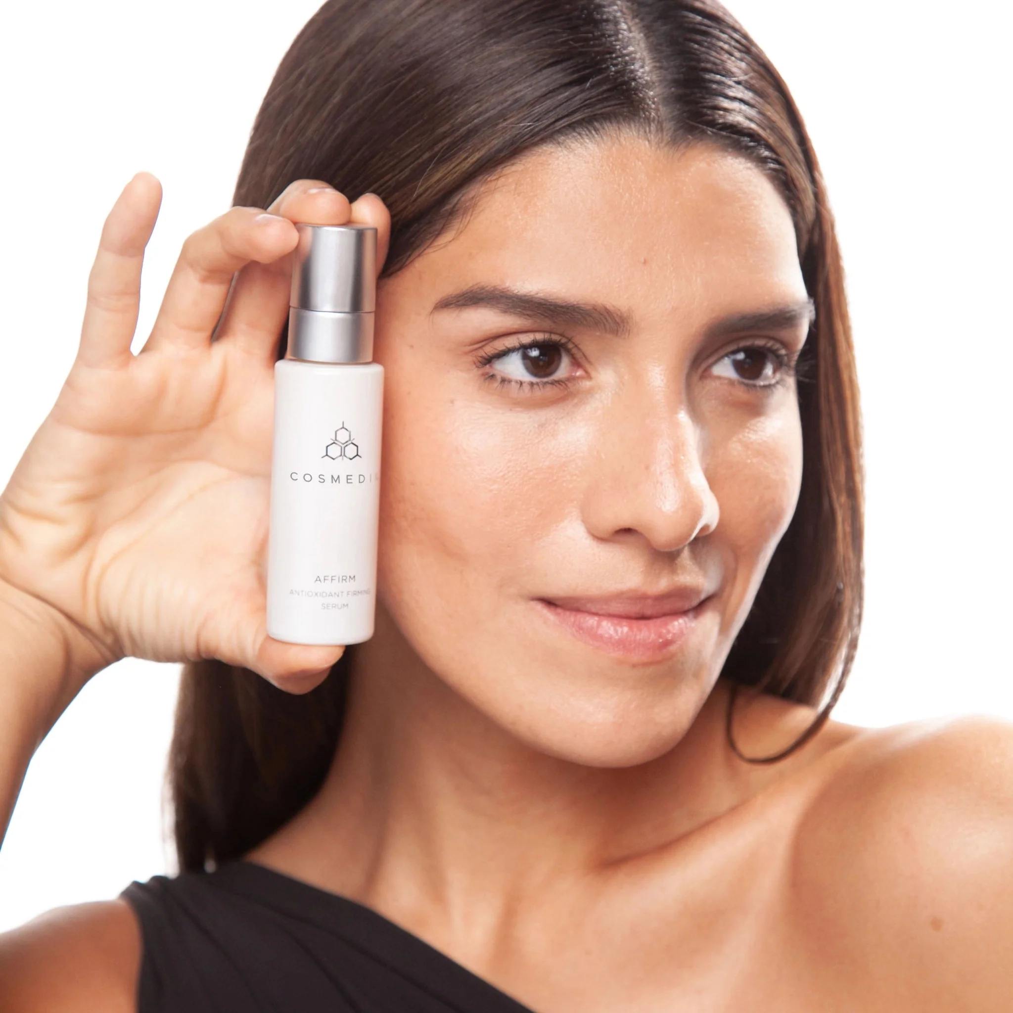 Woman holding Cosmedix Affirm antioxidant firming serum near her face