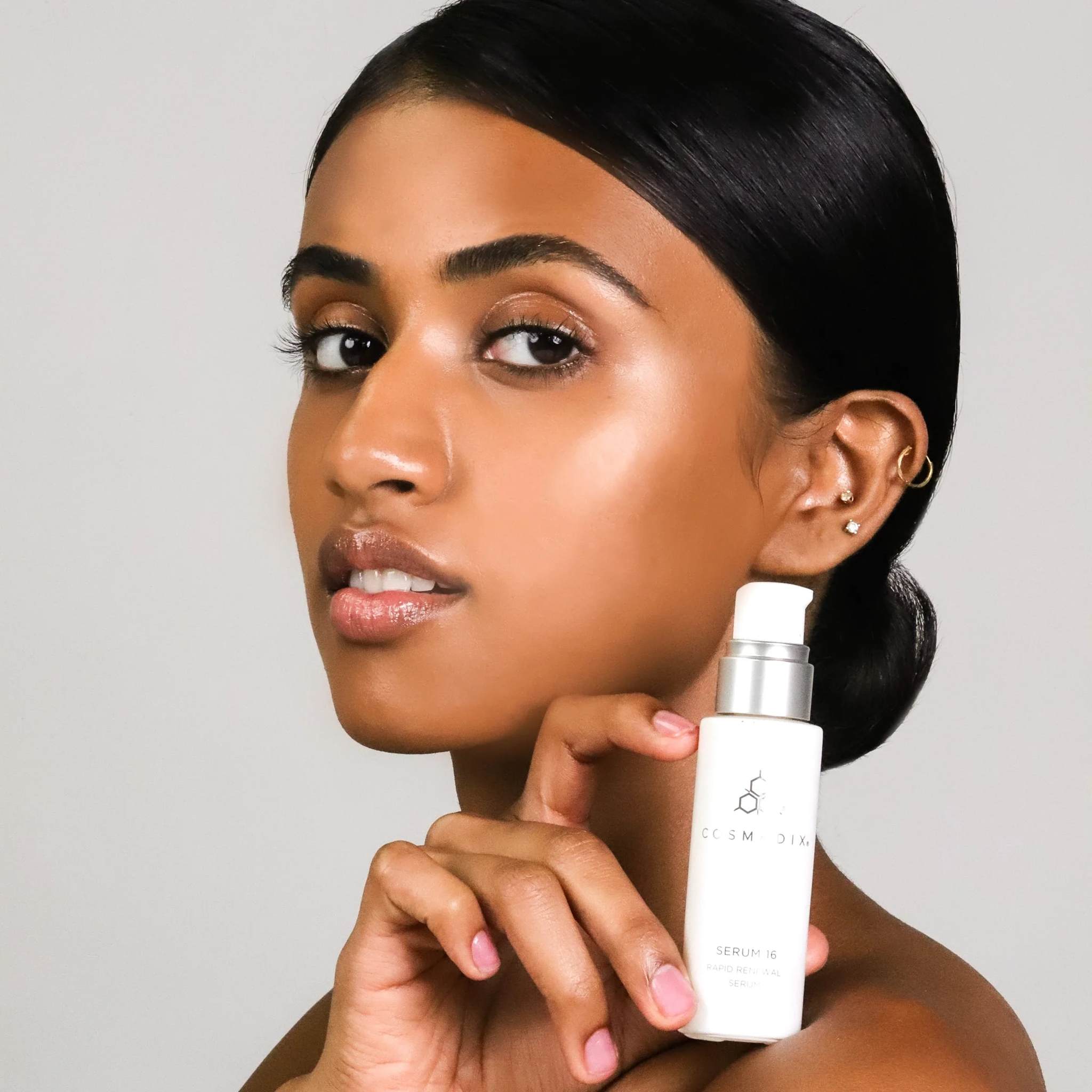 Woman holding Cosmedix Serum 16 rapid renewal serum near her face