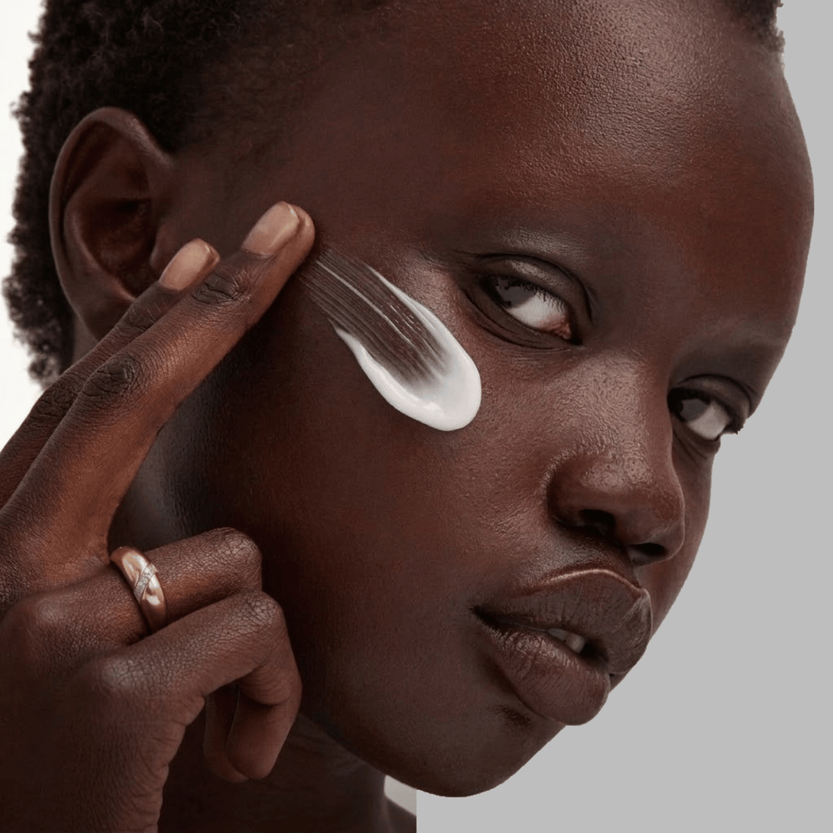 Person applying cream to their face with a neutral background