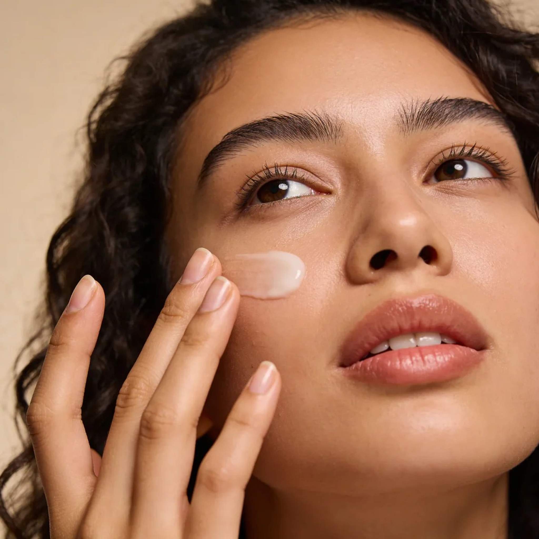 Woman applying Cyspera Sensitive Pigment Corrector rinse-off cream to cheek for gentle dark spot and hyperpigmentation treatment