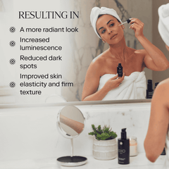 Woman applying Exo C-Serum vitamin C treatment to face in bathroom mirror