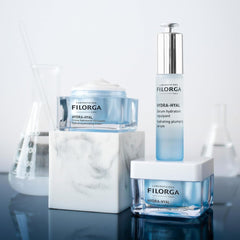 Filorga Hydra-Hyal skincare collection including plumping cream and hydrating serum displayed with laboratory glassware