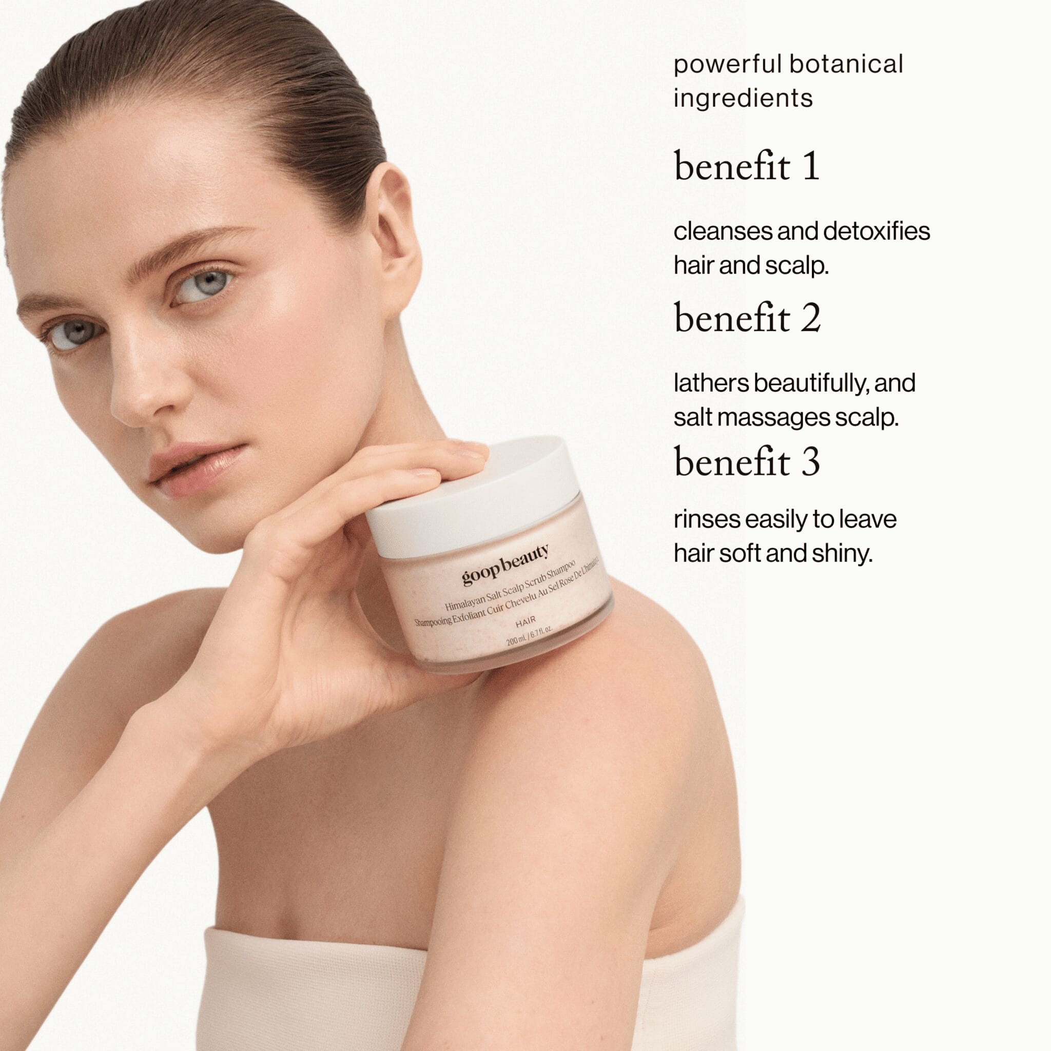 goop beauty Himalayan Salt Scalp Scrub Shampoo held by model highlighting 3 key benefits: cleanses detoxifies and leaves hair soft
