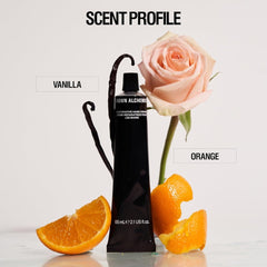 Black tube of Crown Alchemy hand cream with a pink rose and orange slices on a white background, labeled 'Vanilla' and 'Orange'.