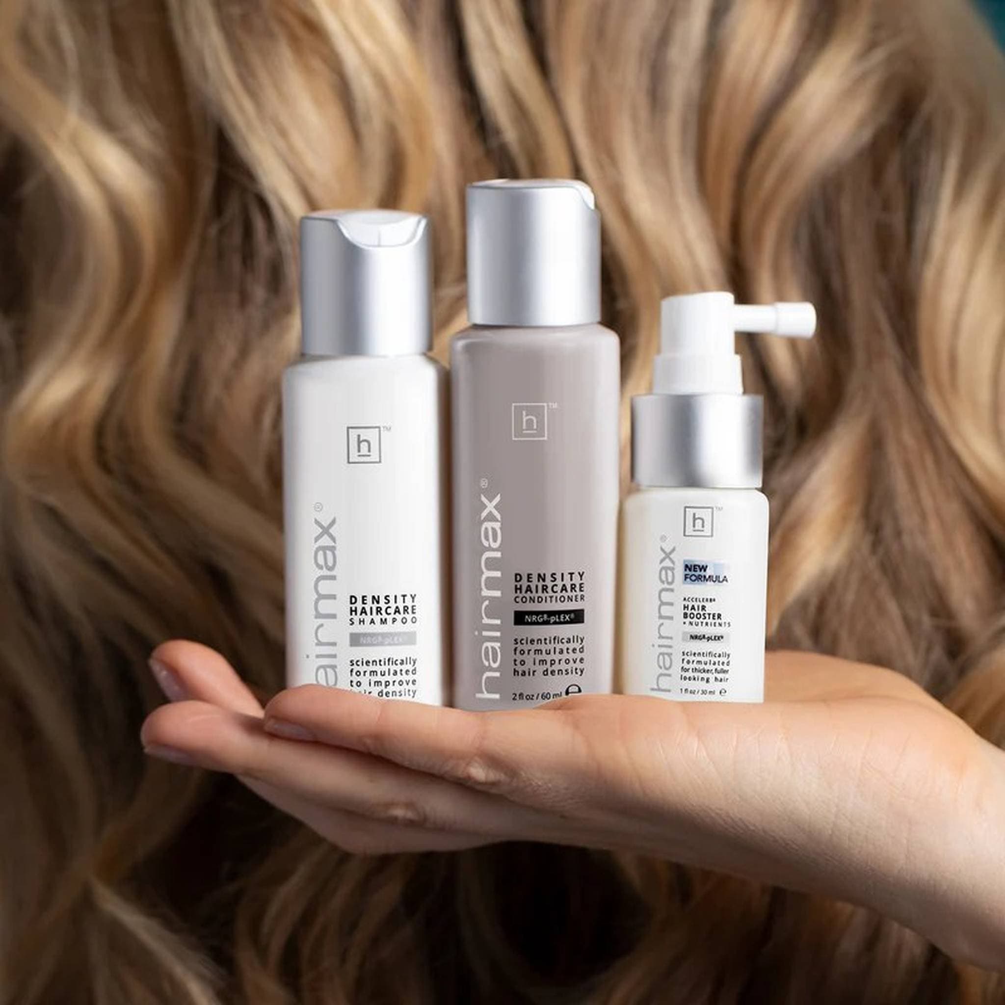 Hand holding Hairmax Density Haircare set against thick wavy blonde hair