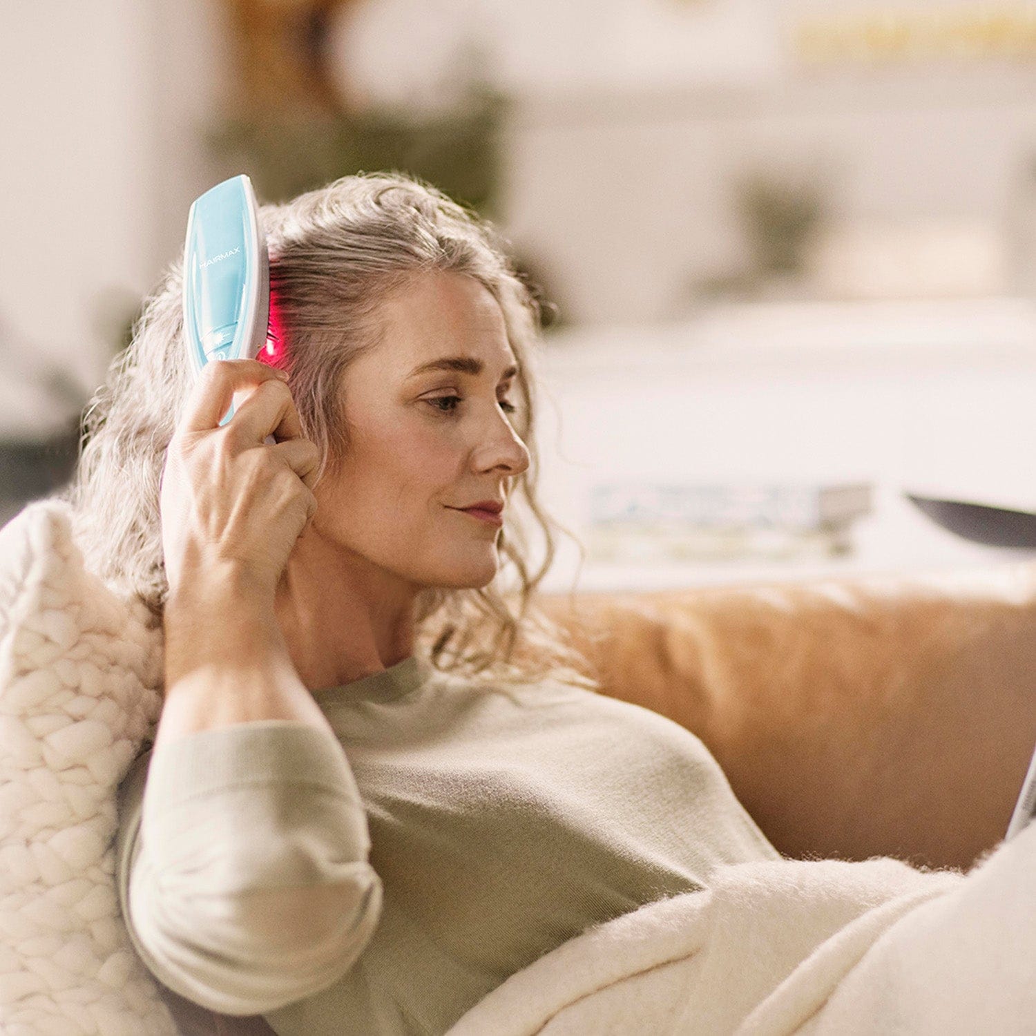 Woman using a hairbrush with LED lights on a blurred indoor background