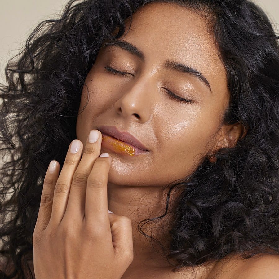 Woman with curly hair applying Henné Organics Lip Mask to her lips for soft nourished hydrated lips