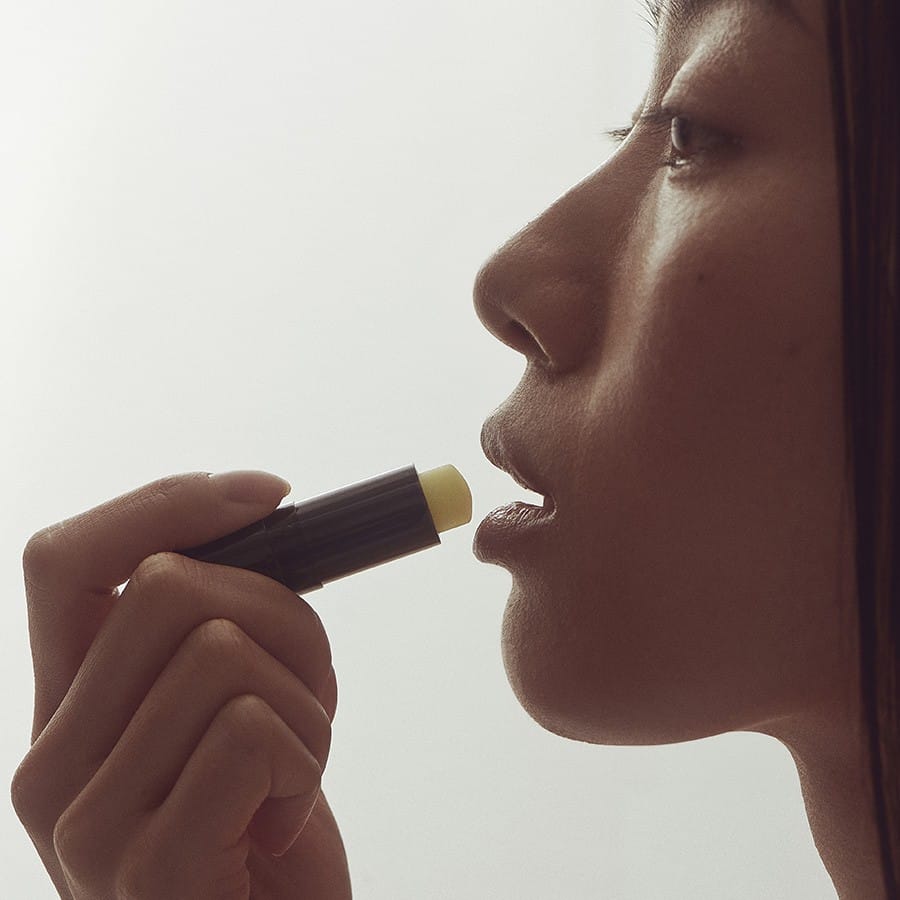 Woman in profile applying Henné Organics Luxury Lip Balm stick to her lips for smooth hydrated lips