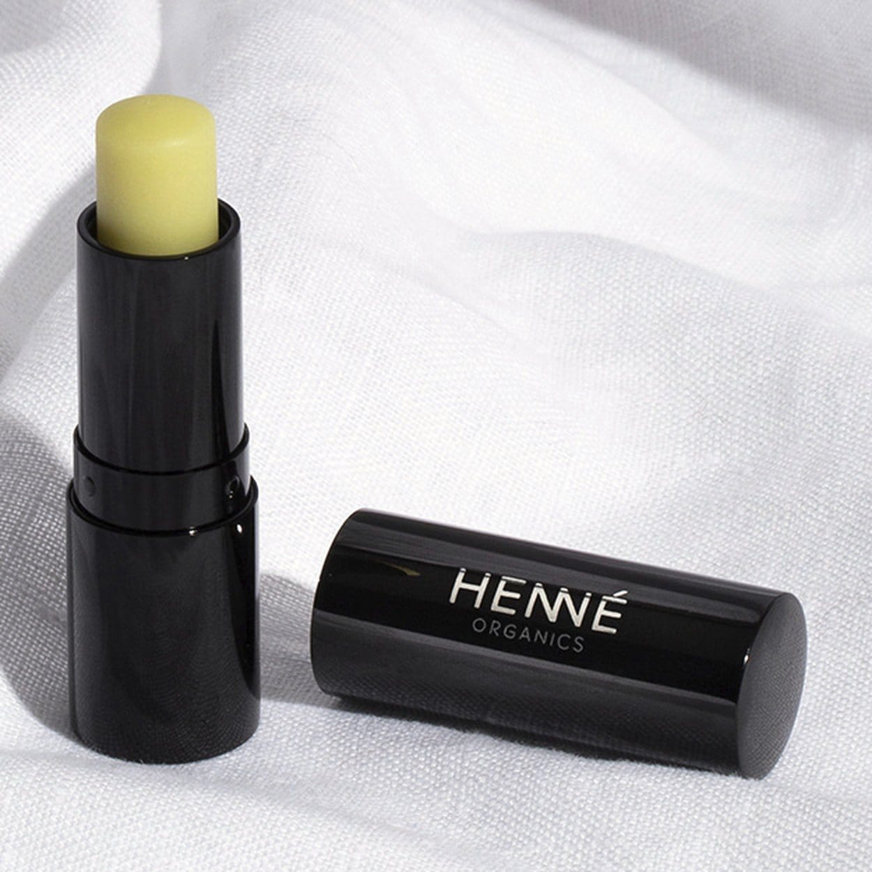 Uncapped Henné Organics Luxury Lip Balm stick and black cap resting on soft white linen